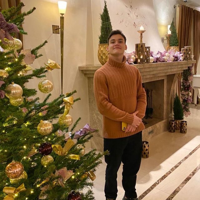 Александр Круг в коричневом свитере рядом с елкой